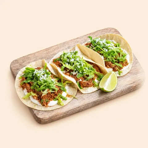 Three chicken tinga tacos on a board
